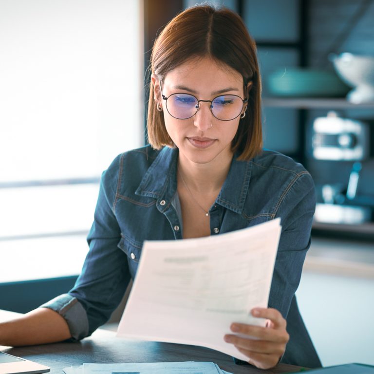 business woman working with computer while consulting some invoices and documents in the kitchen at home.