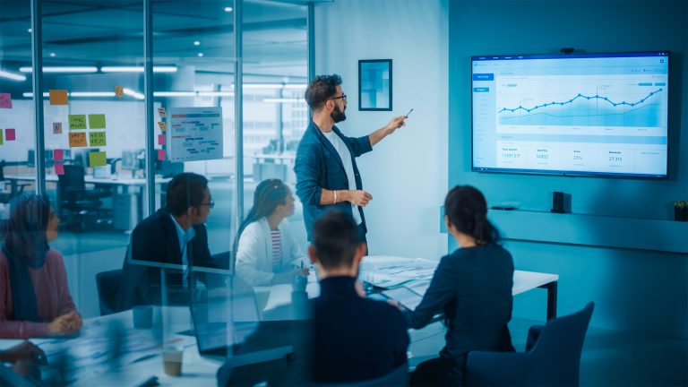 A man presenting a chart to a variety of professional business people